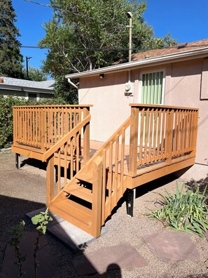 Um deck de madeira com uma escadaria que leva a um edifício com uma porta verde.