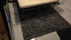 Ein kleines Zimmer mit einer Schlafcouch, einem Klappbett, einem gemusterten Teppich und einer Tür mit Griff.