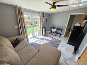 A living room with a sofa, a ceiling fan, a desk, and a view through a glass door to a garden. - Relaxing private entrance suite in pool home (Fort Lauderdale)