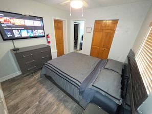 A bedroom with a bed, a dresser, a television mounted on the wall, and a door leading to another room. - Relaxing private entrance suite in pool home (Fort Lauderdale)
