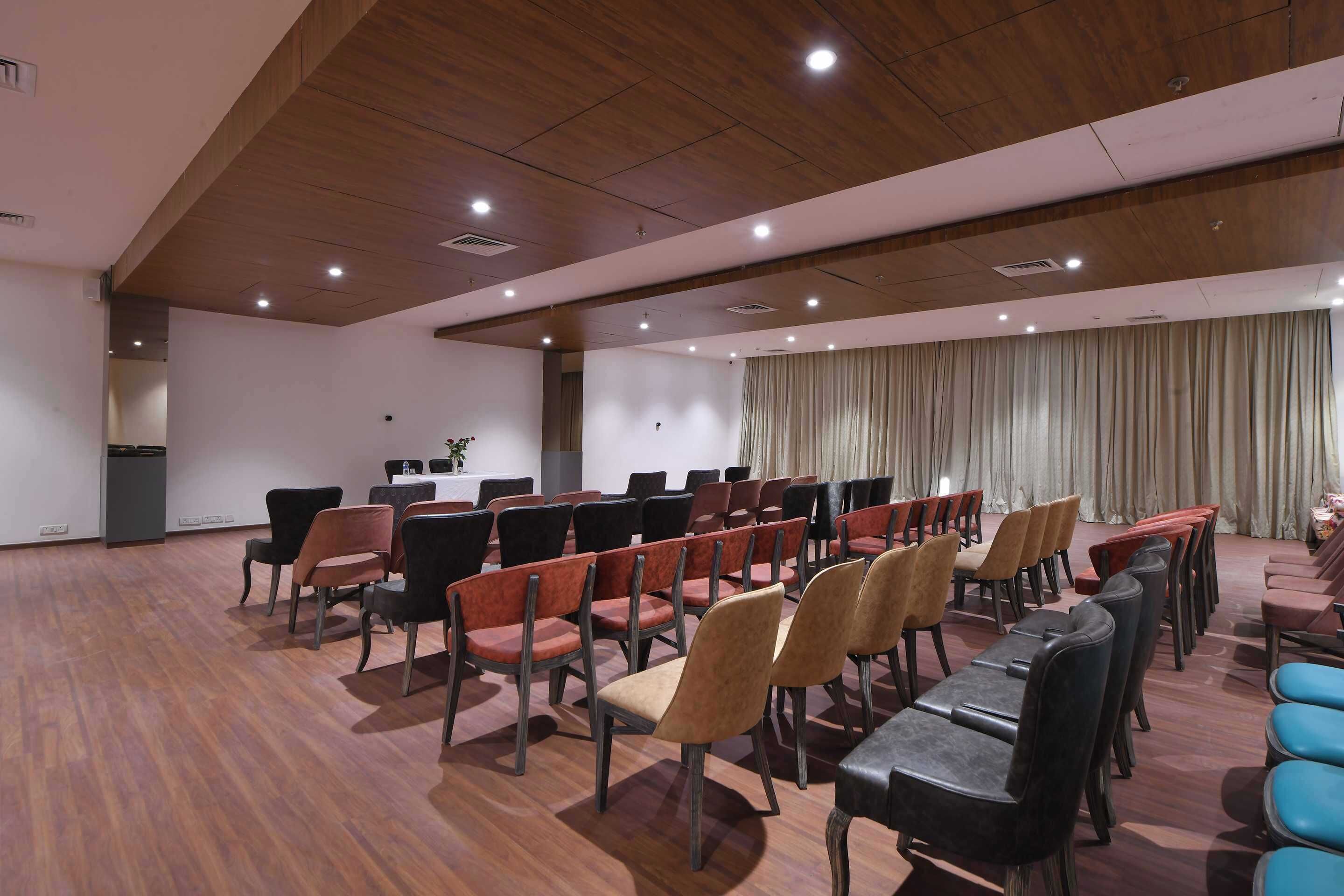 Un salón de conferencias con filas de sillas, un escenario y un telón de fondo.