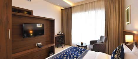 A hotel room with a bed, a TV, a desk with a chair, a sofa, and a window with curtains.