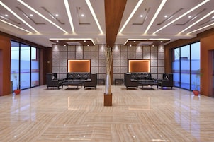 Un lobby amplio con piso de mármol pulido, dos sofás con cojines, un jarrón decorativo y un revestimiento de pared estampado.
