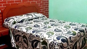 A room with a brick wall, a framed picture, and a bed with a patterned bedspread.