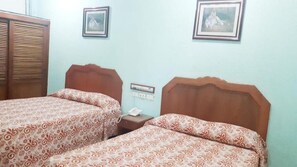 A room with two beds, wooden headboards, patterned bedding, a bedside table with a phone, and framed pictures on the wall. - Hotel Azteca Tabasco  (Villahermosa)