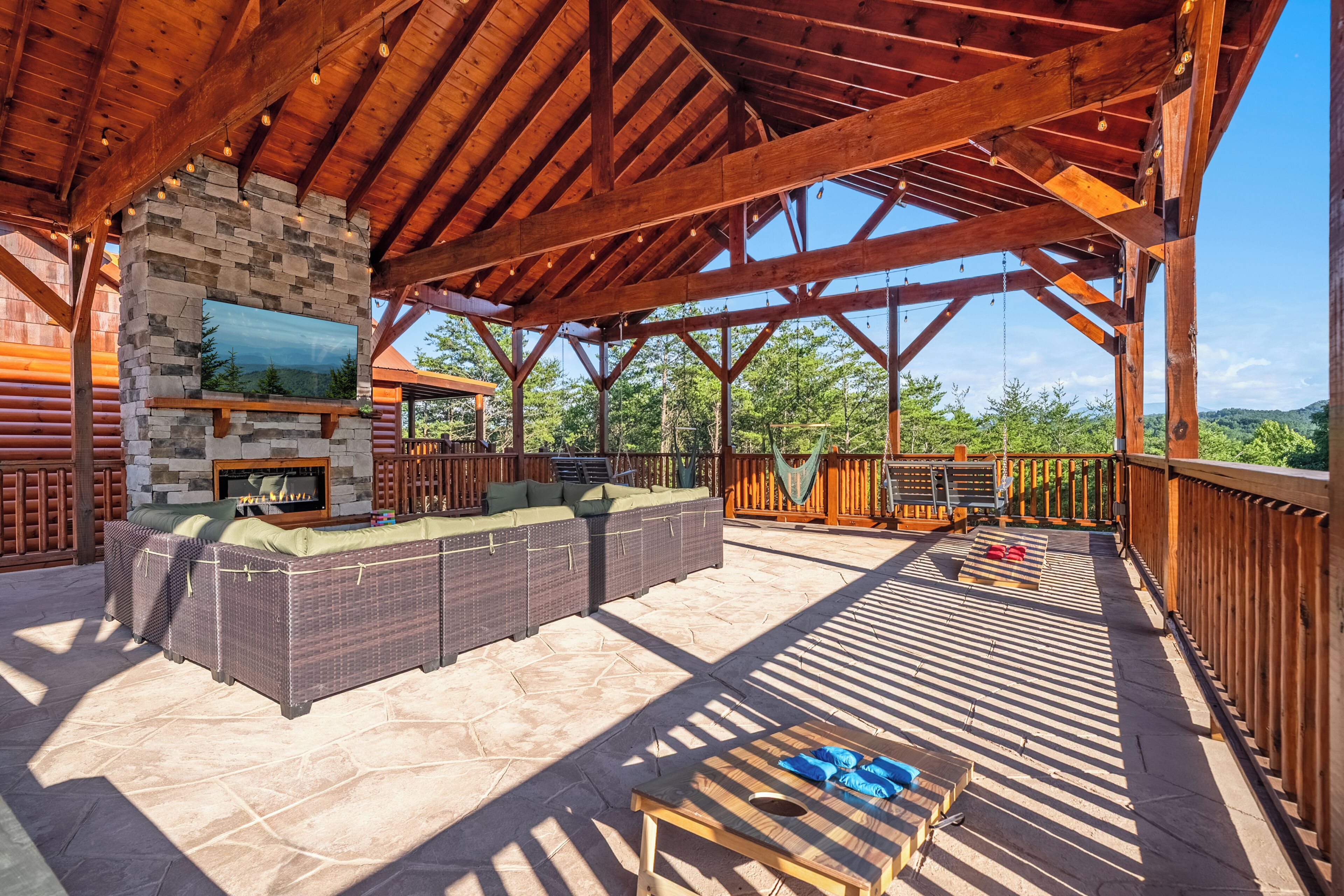 A covered outdoor area with a stone fireplace, wicker furniture, and a view of the surrounding landscape.