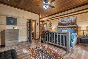 Ein Ferienhaus-Interieur mit Holzbalkendecke, einem Bett mit Kopfteil, einem Schmuckkästchen, einem Schreibtisch und einem Gemälde von einer Berglandschaft.