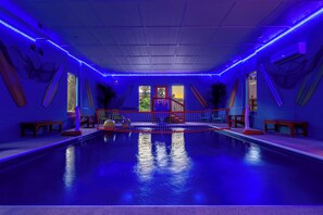 Une piscine intérieure avec un éclairage bleu, un plongeoir et une zone délimitée par un filet.