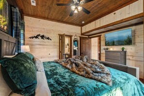 Une chambre à coucher avec un lit, un ventilateur de plafond, une grande fenêtre et une vue sur l’extérieur.