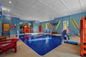 An indoor pool area with a blue pool, a red and white pool net, and surfboards on the wall. - Luxury BRAND NEW 8bdrm Cabin-Pool-Arcades-Gazebo (Sevierville)