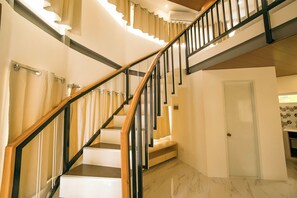 Un escalier avec des marches en bois et des rampes noires, menant à un palier avec une porte blanche et un mur recouvert de carreaux.