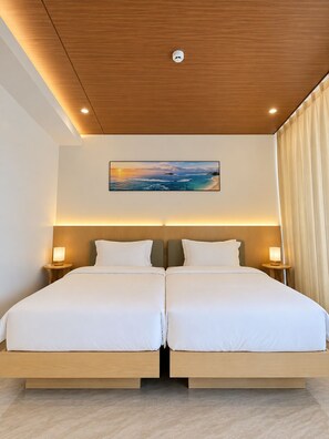 Ein Doppelbett mit Holzkopfteil, zwei Nachttische mit Lampen, ein an der Decke befestigter Rauchmelder und ein gerahmtes Bild eines Sonnenuntergangs über dem Meer.