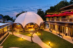 A modern dome-shaped building with an open patio area, surrounded by lush greenery and red umbrellas. - Fizz Diving Resort (Panglao)