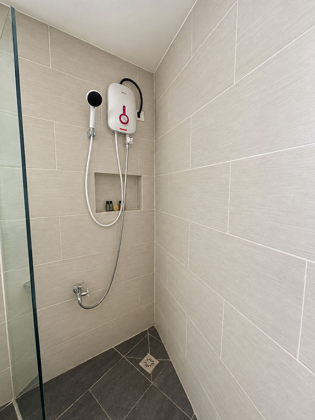 A shower area with a handheld showerhead, a wall-mounted control panel, and a glass partition.