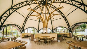 An indoor dining area with high ceilings and a central wooden structure. Tables and chairs are arranged around the space. - Fizz Diving Resort (Panglao)