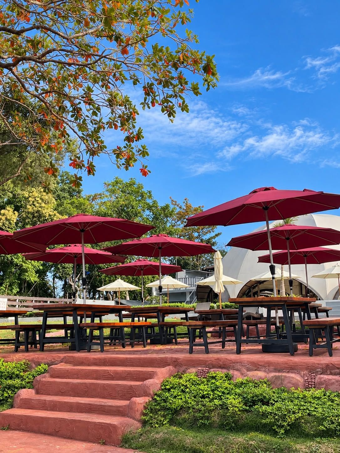 Outdoor seating with red umbrellas, a staircase, and a building with a dome-like structure in the background.