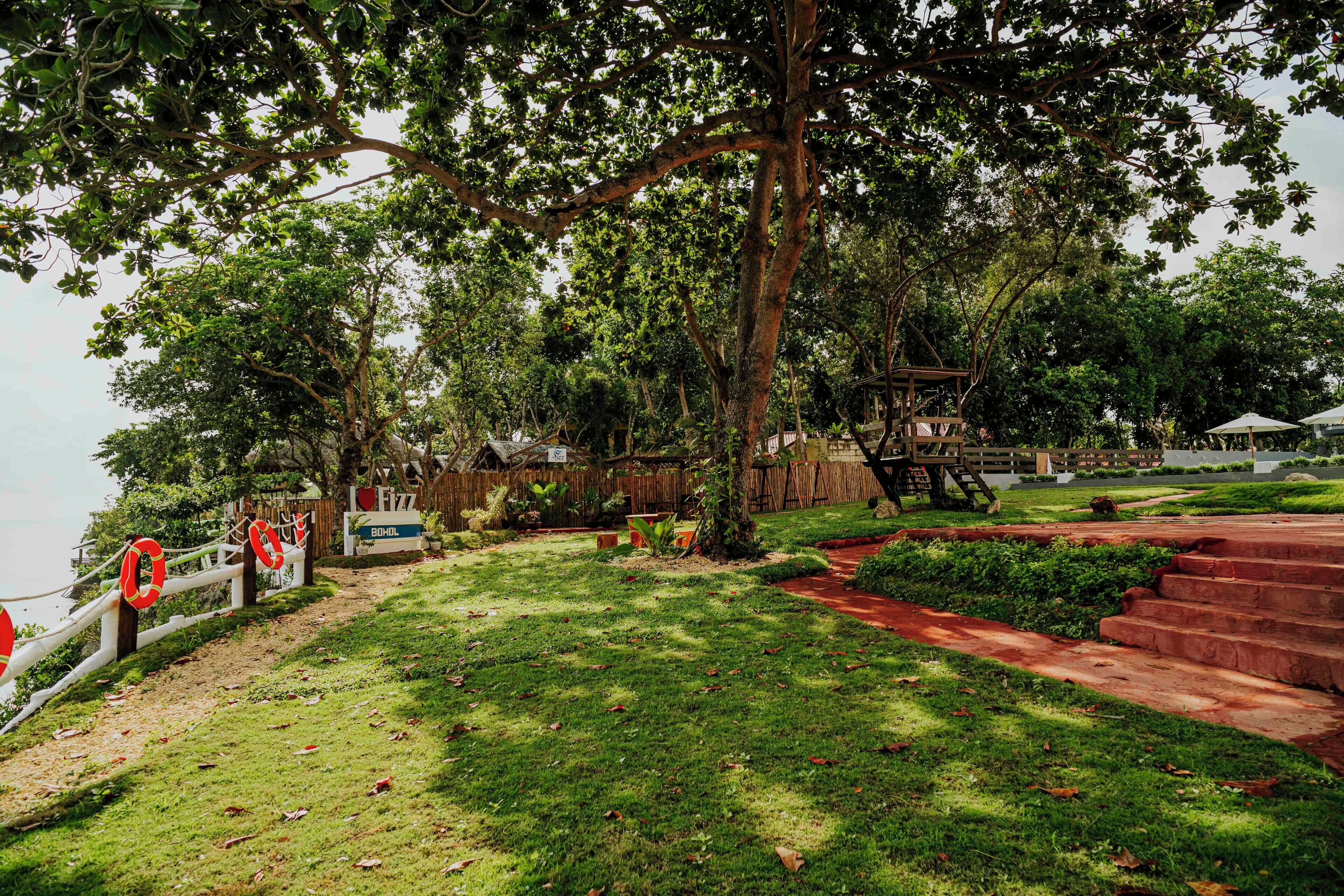 Un parque con una terraza de madera, un letrero que dice 'I love Fizz' y un césped con un camino de ladrillo rojo.
