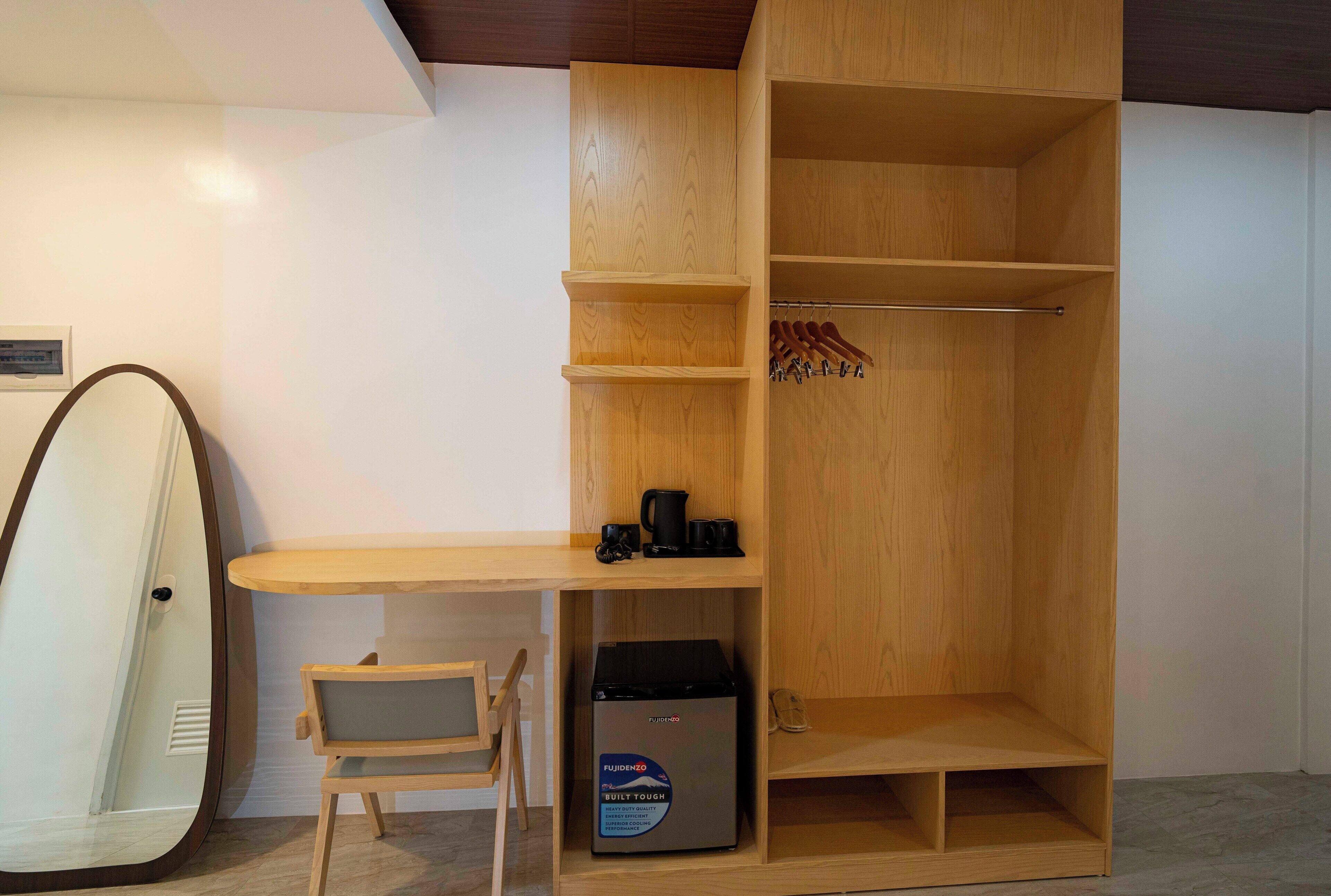 Una habitación pequeña con un escritorio de madera, una silla, un pequeño electrodoméstico negro y un perchero con ganchos.