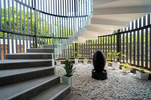 A spiral staircase with a glass railing, surrounded by a pebble-tiled floor and potted plants.