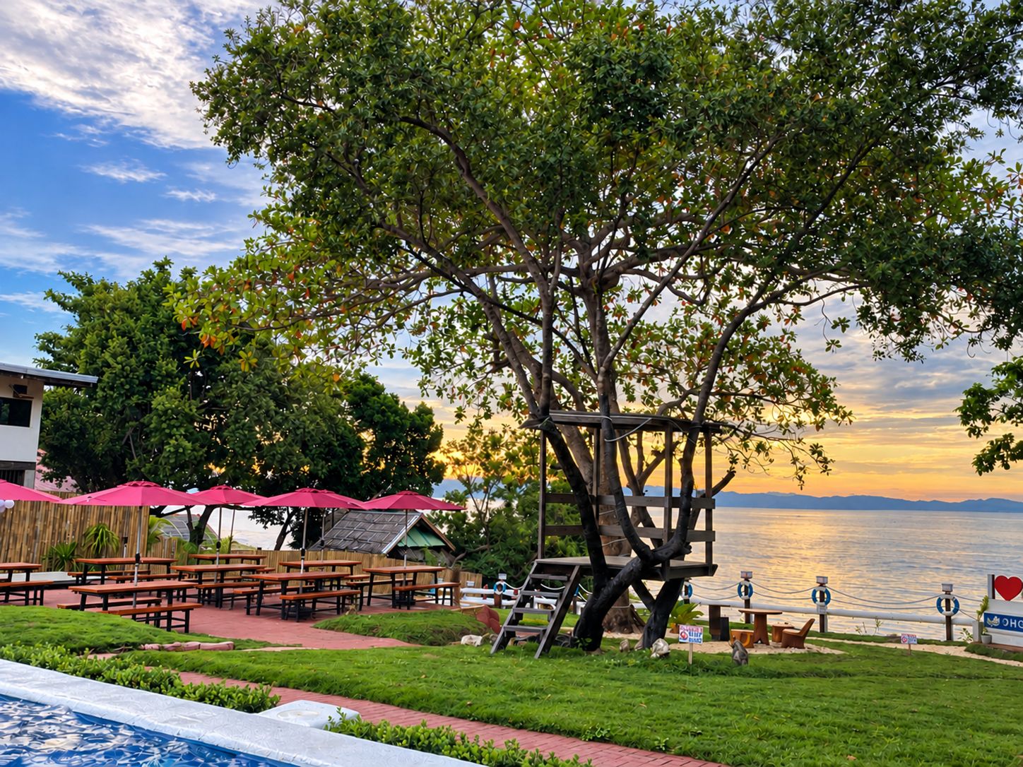 A lakeside patio with picnic tables, umbrellas, and a swimming pool.