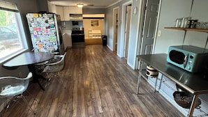 A modern kitchen with wooden flooring, a refrigerator covered in magnets, a microwave, and a dining area with clear chairs. - Lovely 2-bedroom house with AC in Sarasota close to beaches (Sarasota)