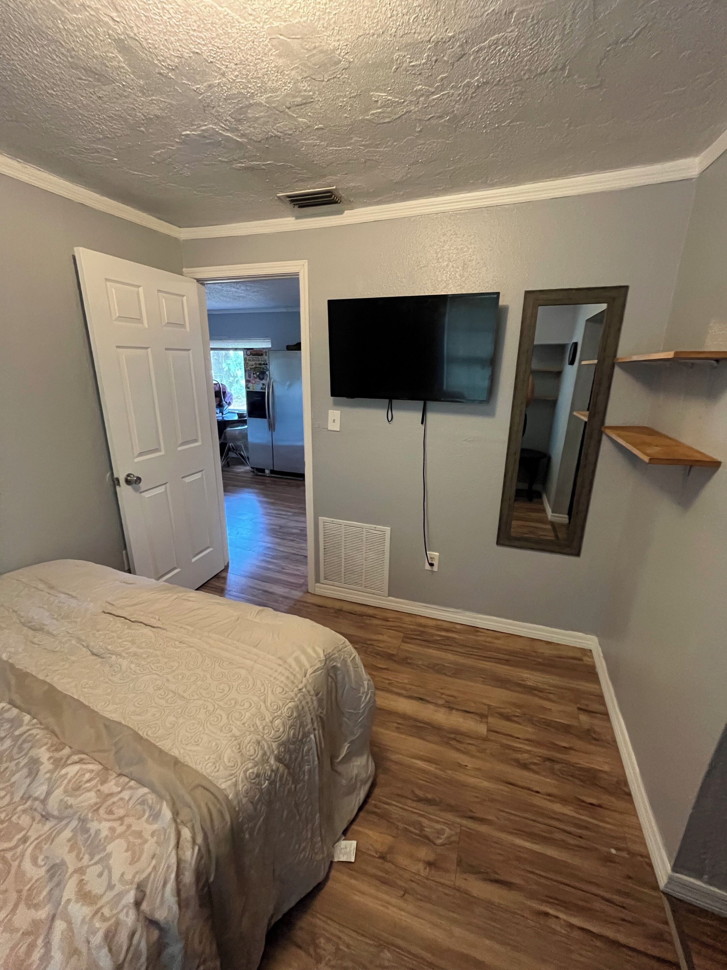 A bedroom with a bed, a television, a mirror, and a hallway leading to another room.