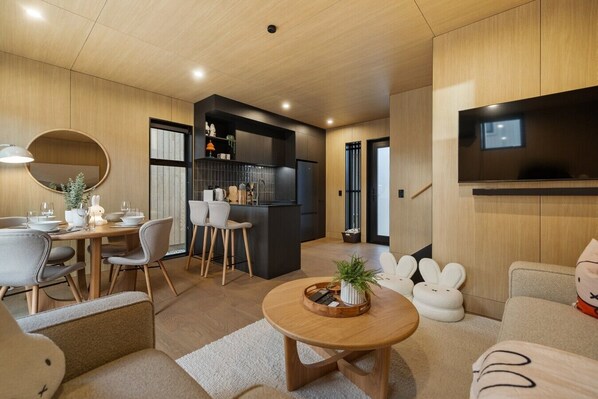 A modern living room with a dining area, kitchen, and a flat-screen TV mounted on the wall.