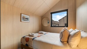 A bedroom with a bed, a window with a view, a framed picture on the wall, and a circular mirror.