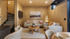 A modern living room with a sofa, chairs, a coffee table, a staircase, and a flat-screen TV.