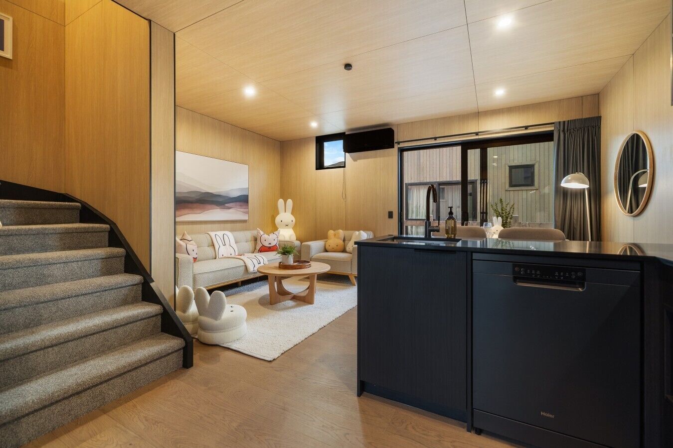 A modern kitchen with a dishwasher, a dining area with a table and chairs, a sofa, and a staircase.