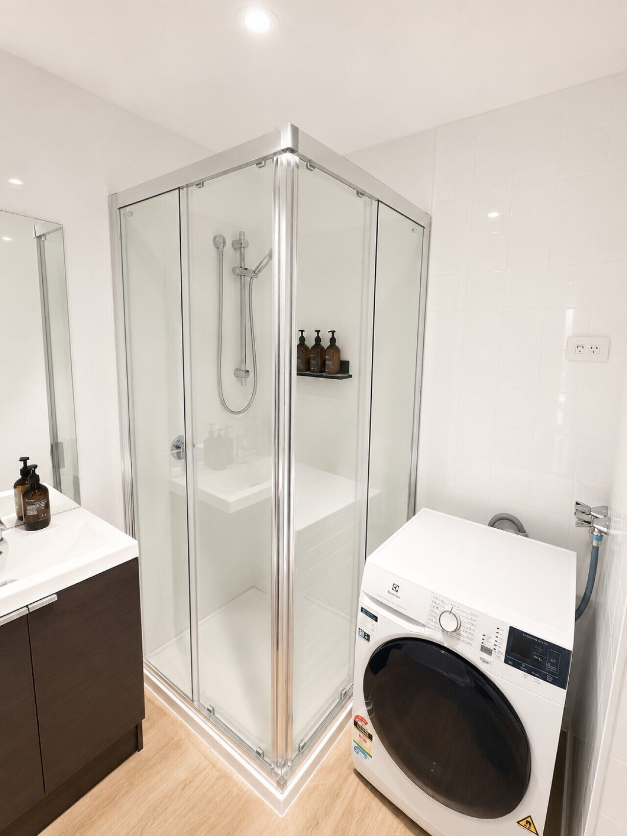 Une salle de bain moderne dotée d’une douche à parois de verre, d’un lave-linge encastré et d’un meuble-lavabo avec miroir.