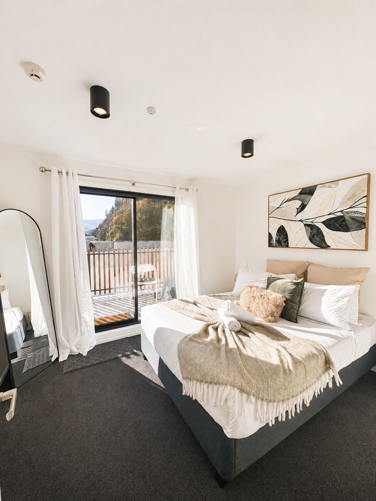 A modern bedroom with a large bed, a view to the outside, and a ceiling light.