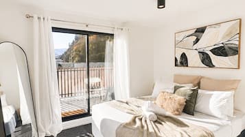 A modern bedroom with a large bed, a view to the outside, and a ceiling light.
