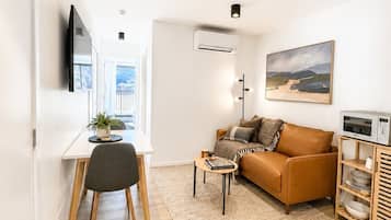 A modern living room with a sofa, a dining table, a TV, and a painting on the wall.