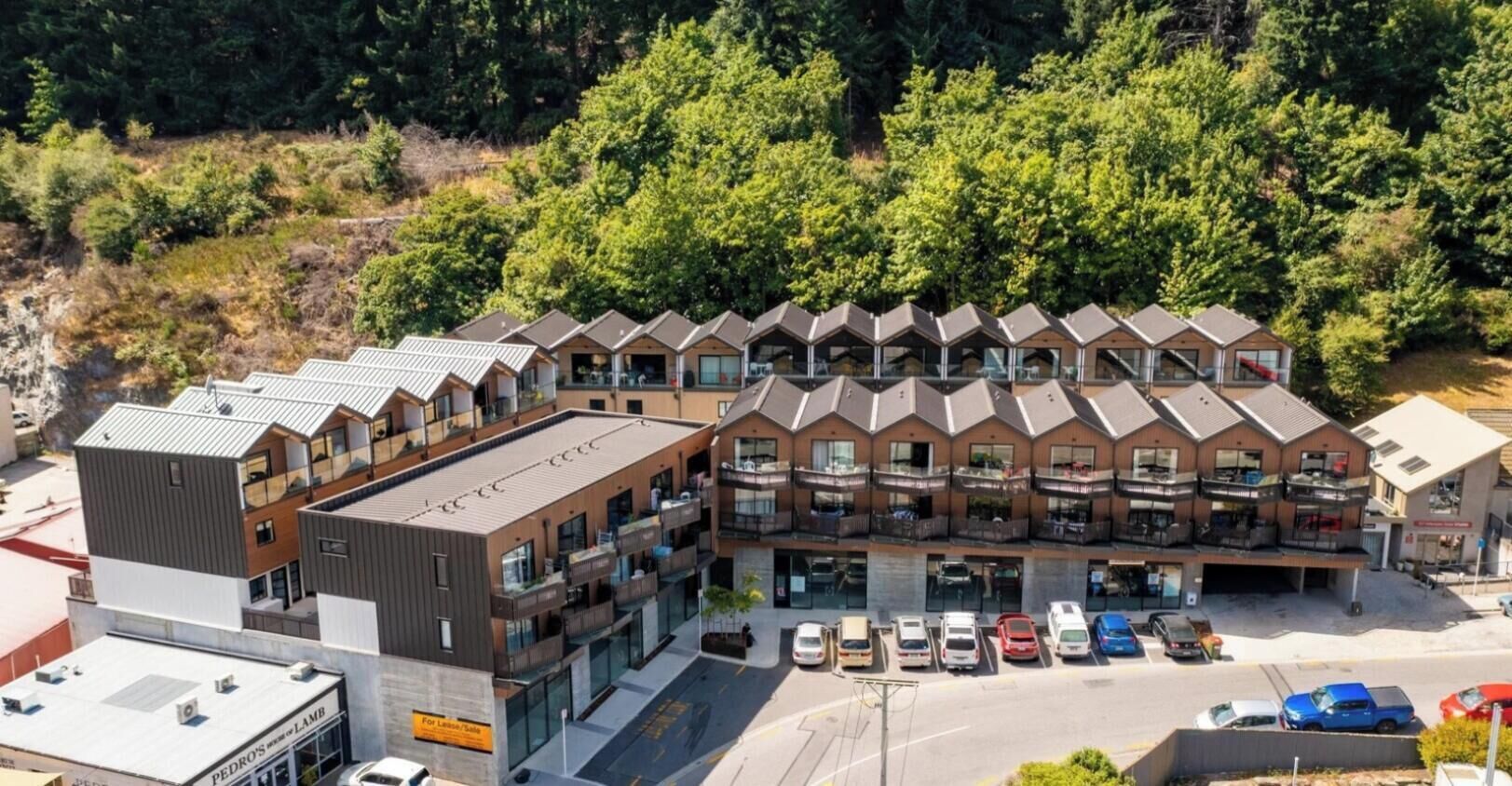 A multi-story hotel with a modern architectural design, featuring balconies and a parking area with several cars.