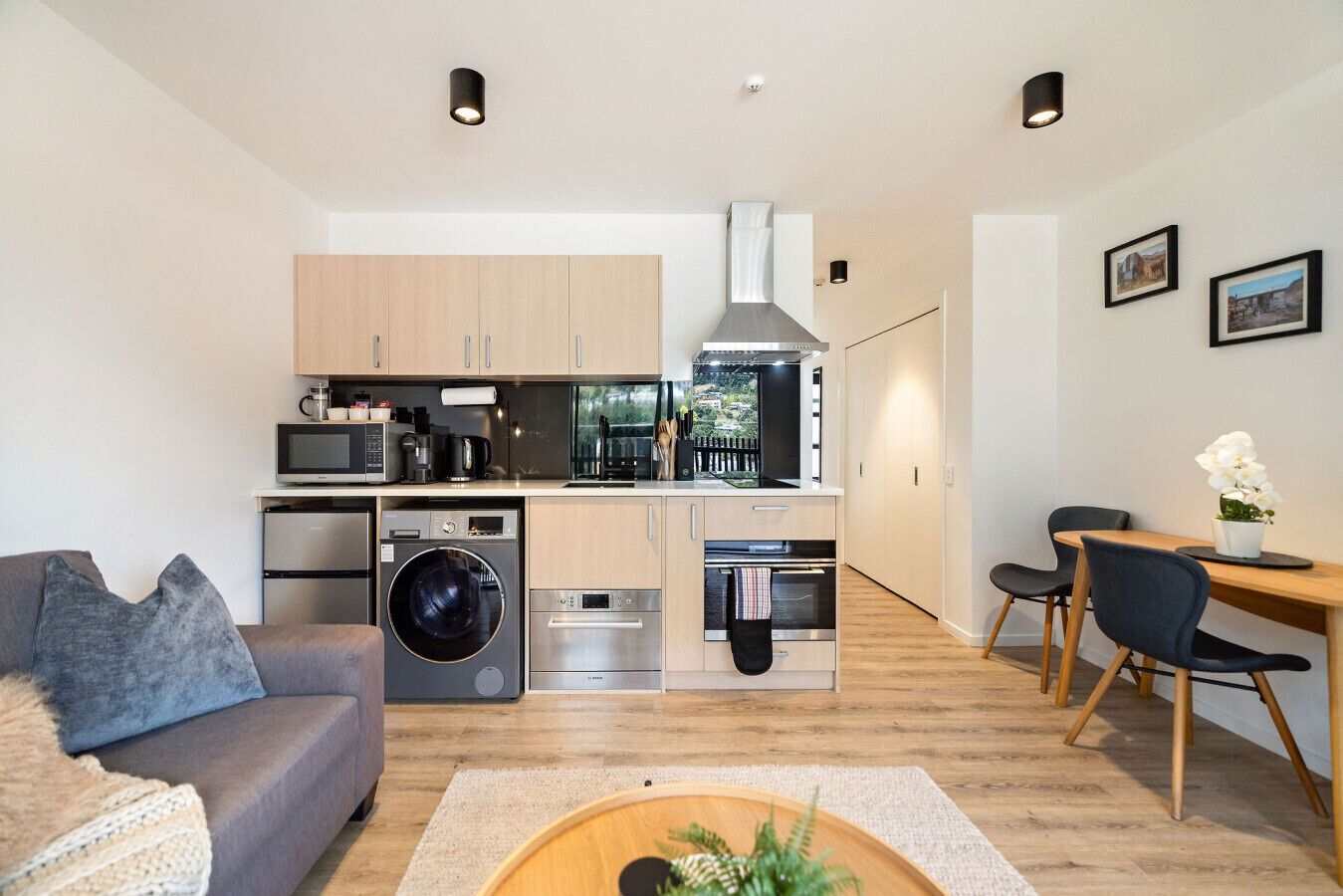 A modern kitchen with stainless steel appliances, a dining area with a wooden table and chairs, and a living room with a sofa and a coffee table.