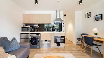 A modern kitchen with stainless steel appliances, a dining area with a wooden table and chairs, and a living room with a sofa and a coffee table.