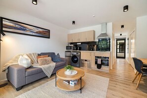 Un appartement moderne avec un canapé gris, une table basse ronde, une cuisine dotée de meubles en bois et un coin repas.