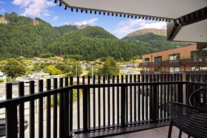Un balcon donnant sur un paysage montagneux, une route avec des véhicules et un bâtiment moderne doté de balcons.
