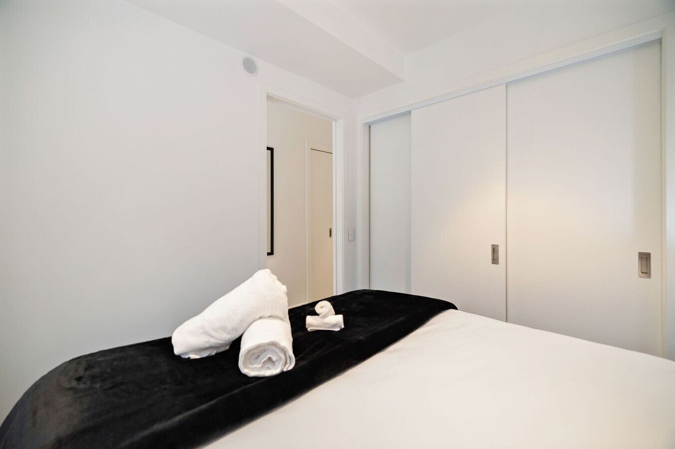A hotel room with a bed, a black headboard, white walls, and a door.