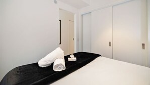 Hotellihuone, jossa on sänky, musta pääty, valkoiset seinät ja ovi.