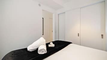 A hotel room with a bed, a black headboard, white walls, and a door.