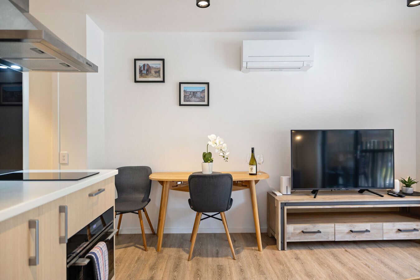 A modern kitchen with a dining area, a flat-screen TV, and two framed pictures on the wall.