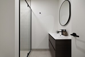 A modern bathroom with a glass shower enclosure, a white sink with dark cabinetry, and a round mirror on the wall. - Prime Location with mountain views (Queenstown)