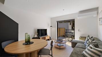 A modern living room with a dining area, a sofa, a TV, and a small table with a lamp.