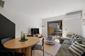 A modern living room with a dining area, a sofa, a TV, and a small table with a lamp. - Prime Location with mountain views (Queenstown)