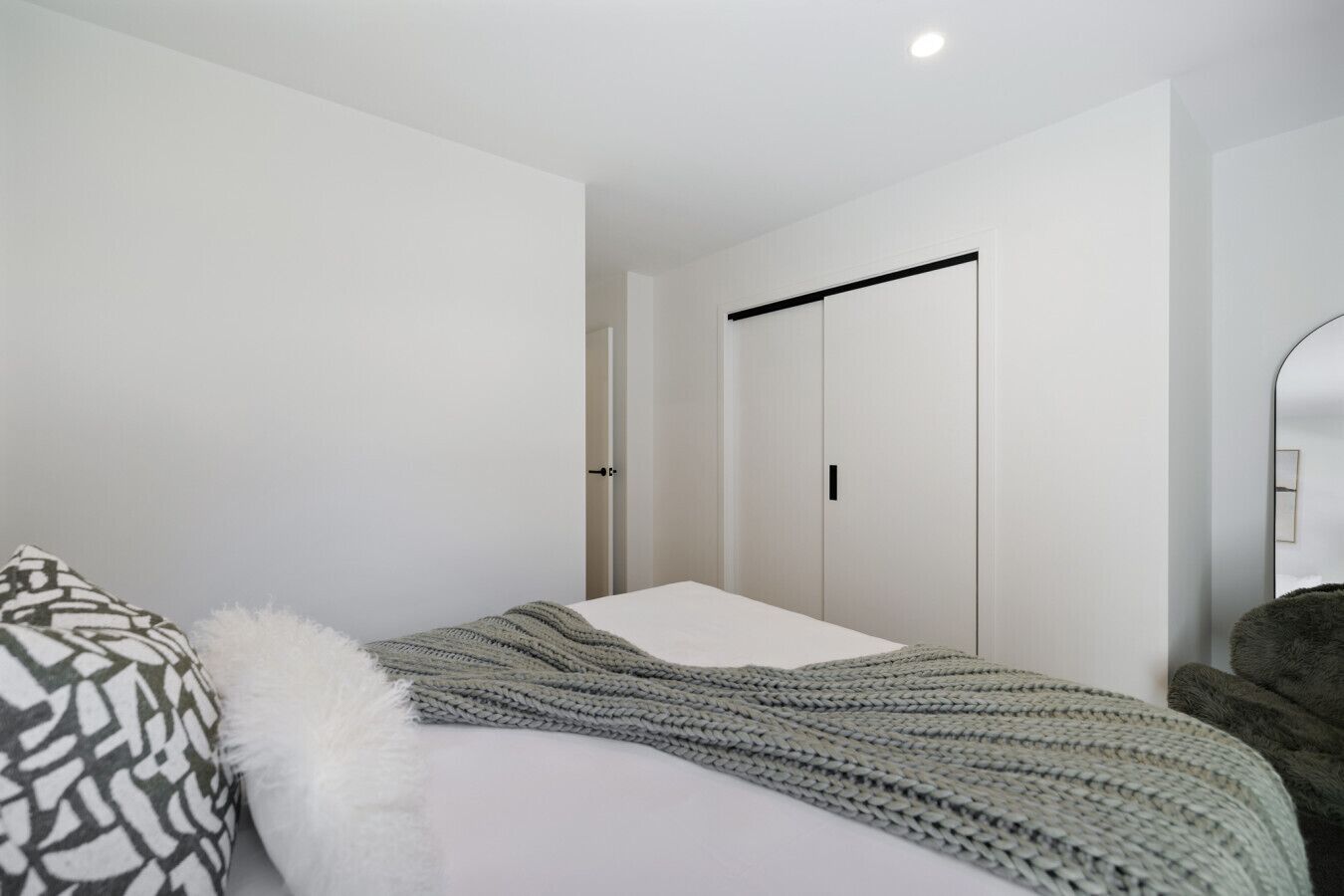 A minimalist bedroom with a bed, a wardrobe, and a mirror.