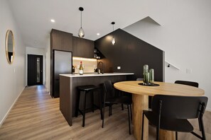 A modern kitchen with a central island, black bar stools, and a round wooden table with chairs. - Prime Location with mountain views (Queenstown)