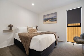 A bedroom with a bed, a nightstand, a lamp, a painting, a sliding door, and a chair. - Prime Location with mountain views (Queenstown)