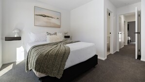 A modern bedroom with a large bed, a painting above the bed, and a hallway leading to other rooms. - Prime Location with mountain views (Queenstown)